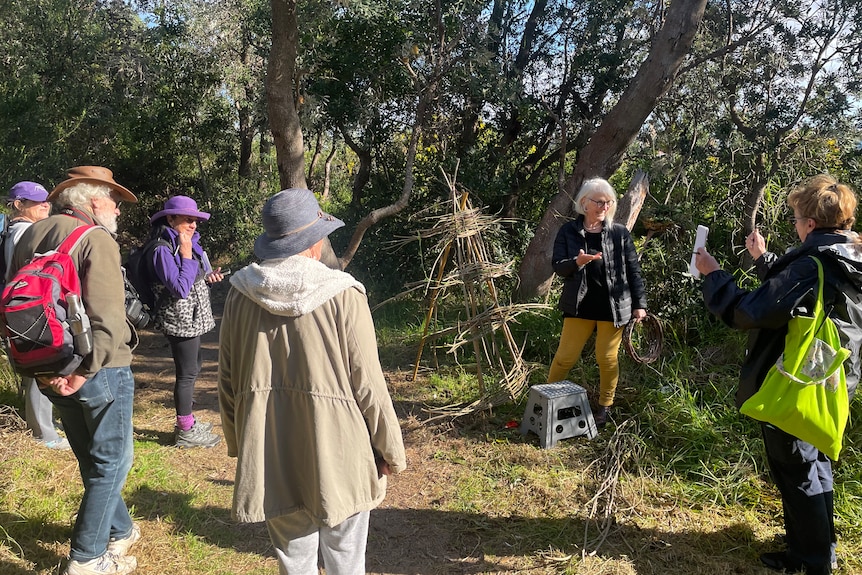 Group of walks watch an artist create a sculpture out of twigs and leaves