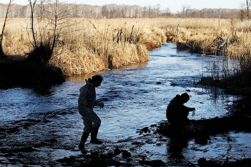 Two men walk in the shallows of the Techa River with scientific equipment.