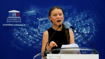 Greta Thunberg speaking at a lectern with the French Assemblee Nationale logo on it.
