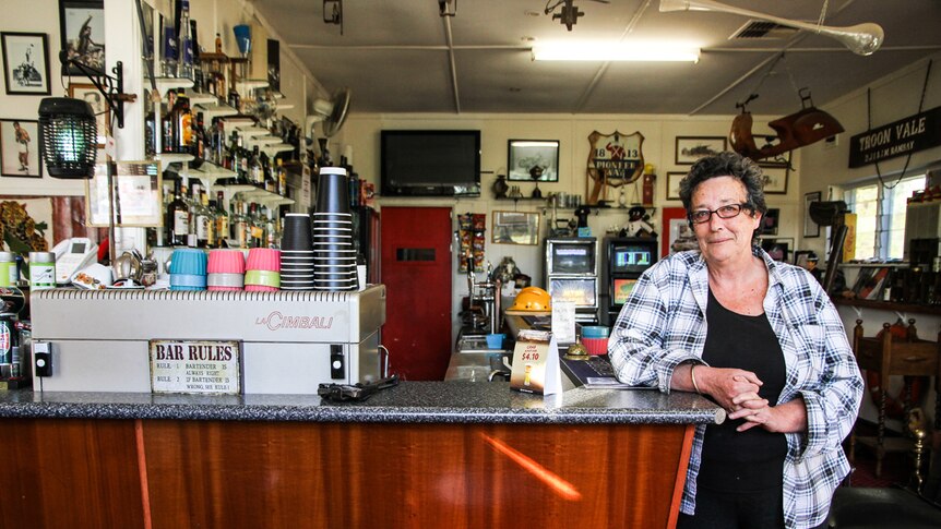 A woman in a flannel shirt stands next to the bar, which has an espresso machine behind it.