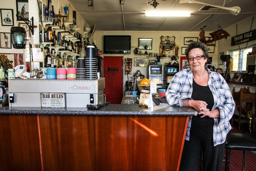 A woman in a flannel shirt stands next to the bar, which has an espresso machine behind it.