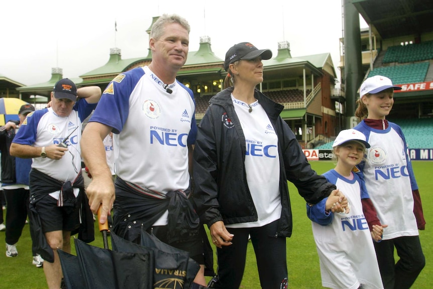 Former cricketer Dean Jones walks on a stadium green with his wife and two young daughters all wearing matching shirts