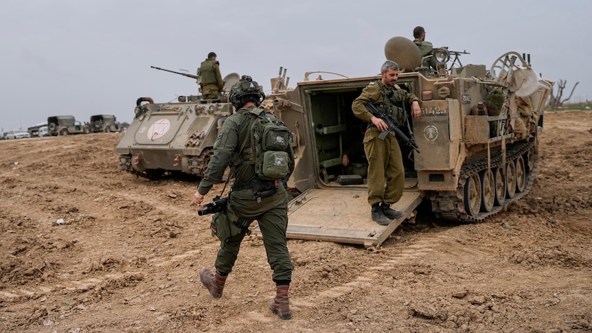 Israeli soldiers are seen at a staging area near the Israeli-Gaza border, walking near military vehicles.