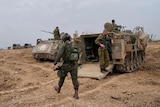 Israeli soldiers are seen at a staging area near the Israeli-Gaza border, walking near military vehicles.