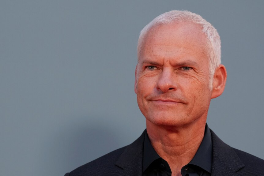 Martin McDonagh smiles in front of a pale blue background