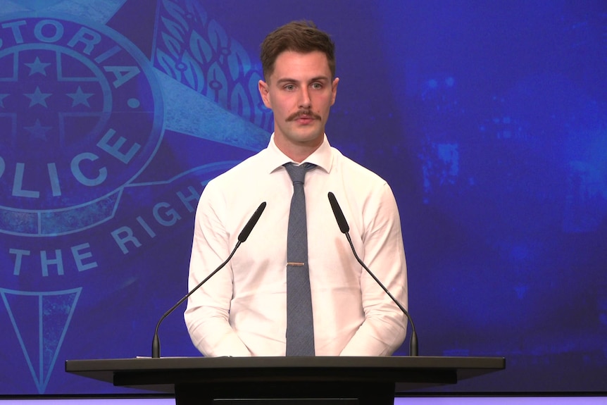 A man in a shirt and tie in front of a victoria police logo