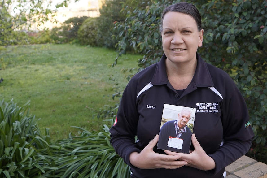 woman sitting, holding a photo of her father