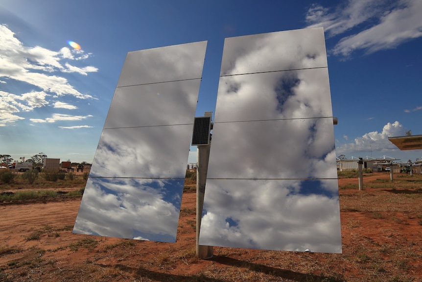 Two large mirrors sitting on a pole, with a dirt landscape in the background.