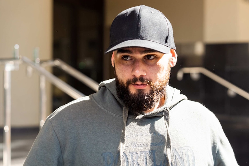 A man in a black hat and grey hoodie leaves court