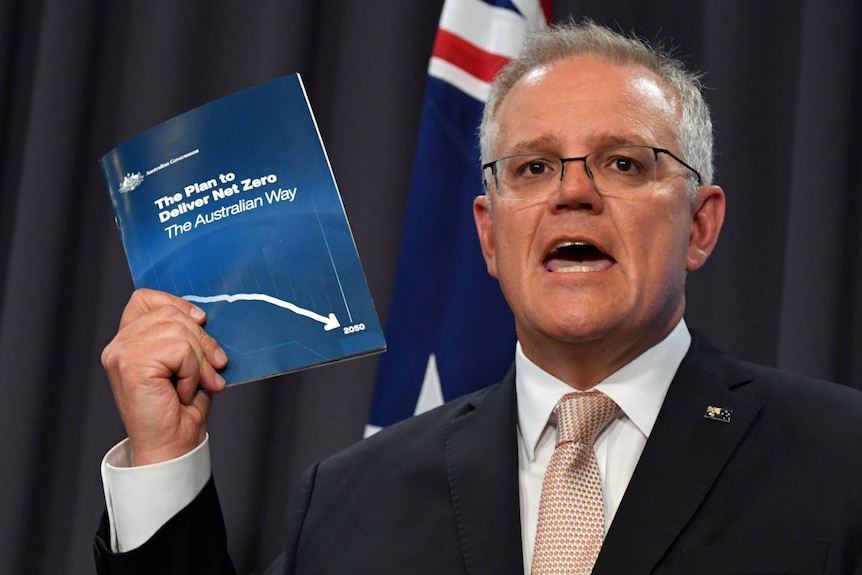 A man wearing a suit holds up a blue booklet.