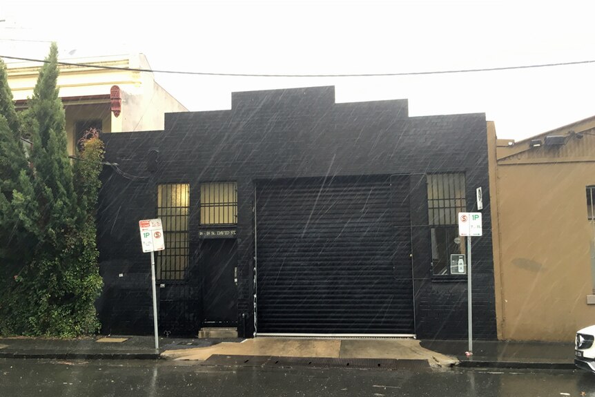Factory exterior, black-painted walls with a garage door open to show a forklift inside.