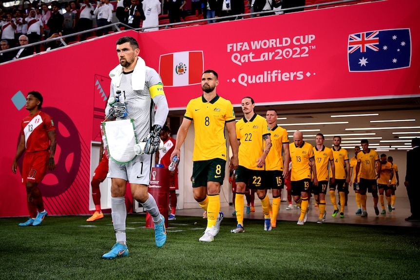 Australia's Socceroos emerge onto the field for a game, passing under a sign saying 'FIFA World Cup Qatar 2022'.