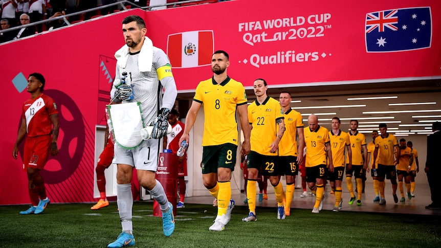 Australia's Socceroos emerge onto the field for a game, passing under a sign saying 'FIFA World Cup Qatar 2022'.