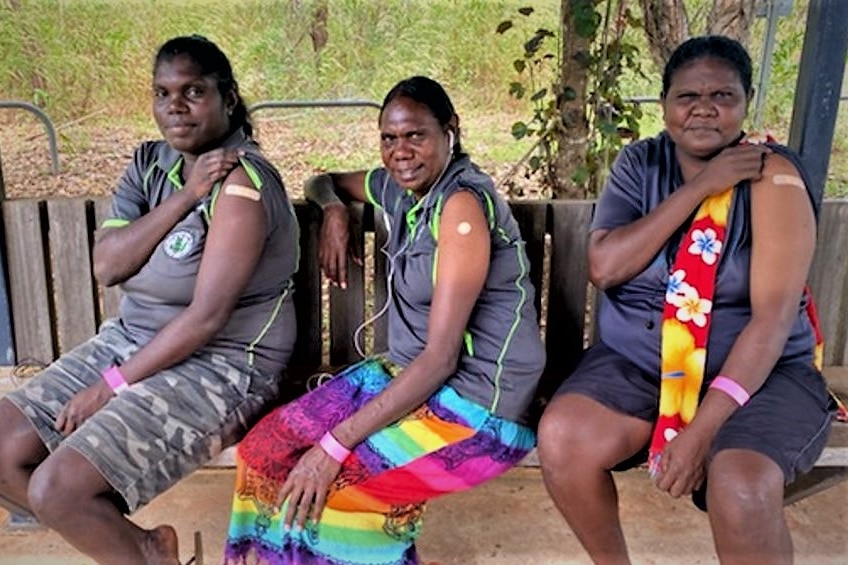 Three women posing for a photo with their sleeves rolled up showing a bandage.