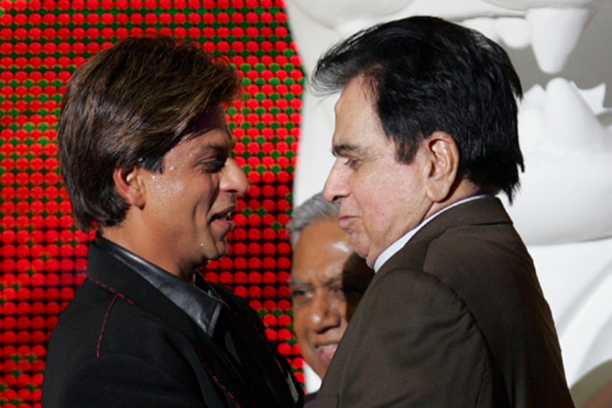 A wait shot of Dilip Kumar  and Shah Rukh Khan facing each other hugging on the red carpet. 