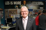 Les Murray stands in the office with a promo poster for Les is More on the back wall.