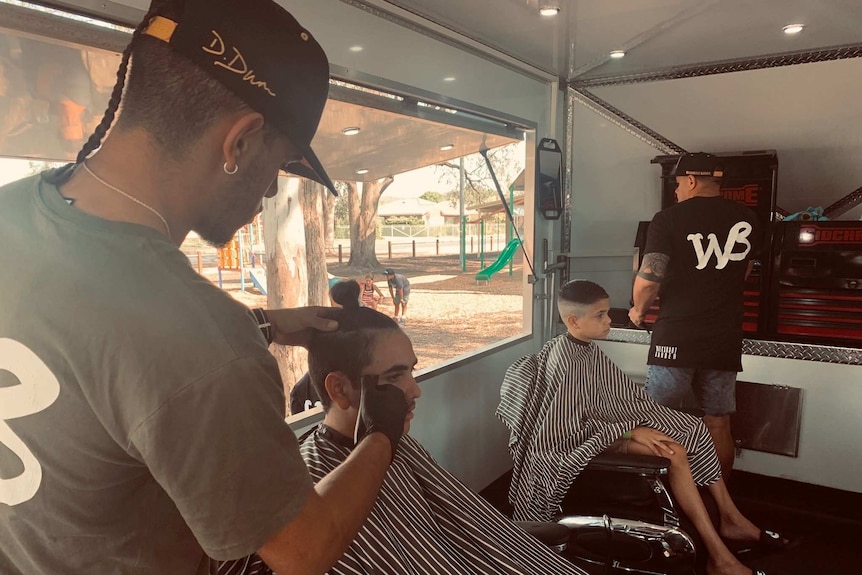 A barber cuts a boy's hair in a mobile barber shop.