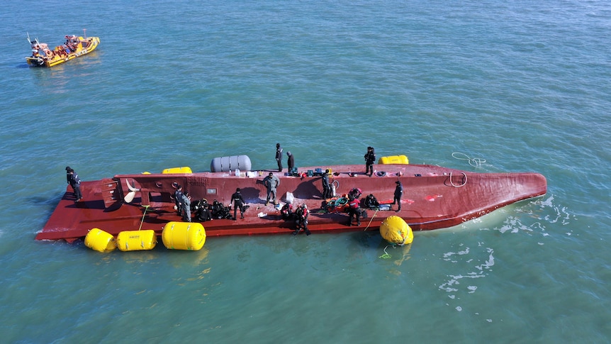 upside down boat in the ocean with rescue crews 