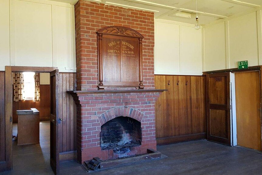 The rundown interior of an old church, including a fireplace and wooden honour board