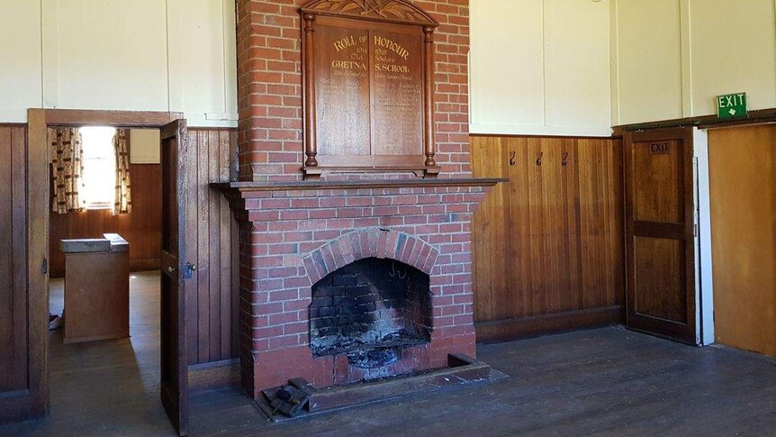 The rundown interior of an old church, including a fireplace and wooden honour board