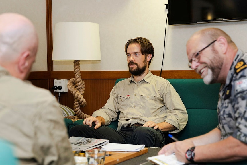 A man sits on a couch next to a man in a Navy uniform