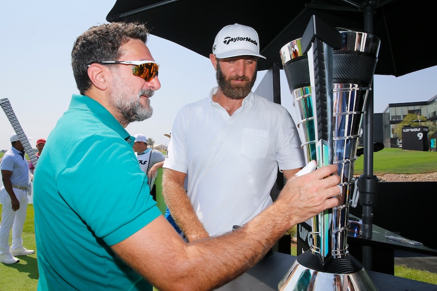 Yasir Al Rumayyan speaks to Dustin Johnson while holding the trophy at a LIV Golf event