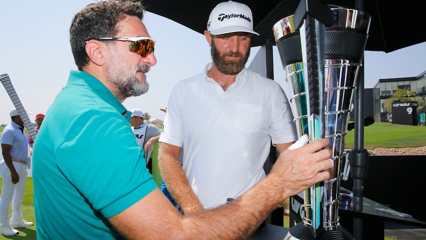 Yasir Al Rumayyan speaks to Dustin Johnson while holding the trophy at a LIV Golf event