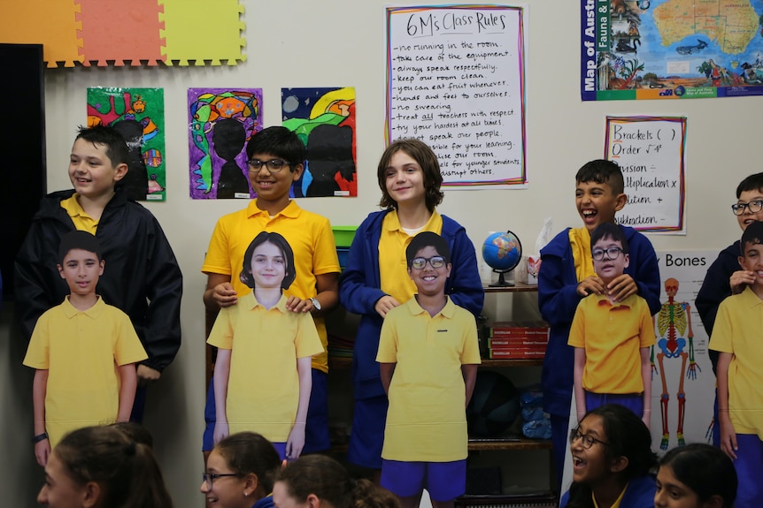 Primary school students holding cardboard cutouts of their classmates.
