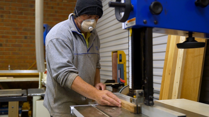 A man in a beanie using a buzz saw.