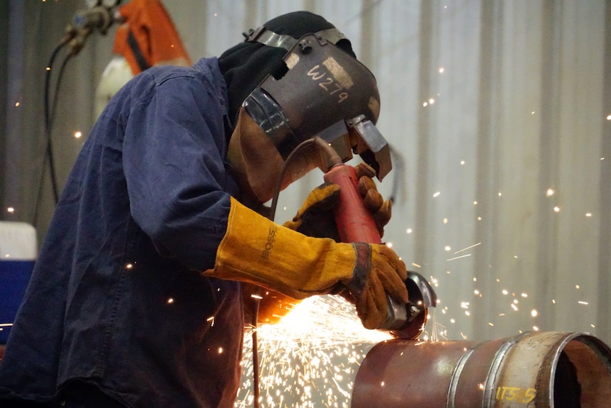 Sparks fly as a worker using a grinder cuts a pipe.
