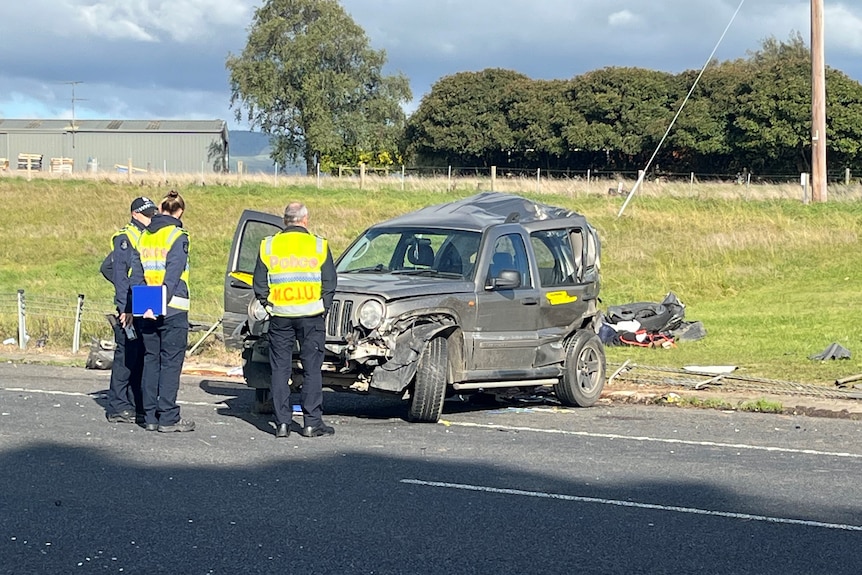 Three police inspecting a crashed SUV on the highway