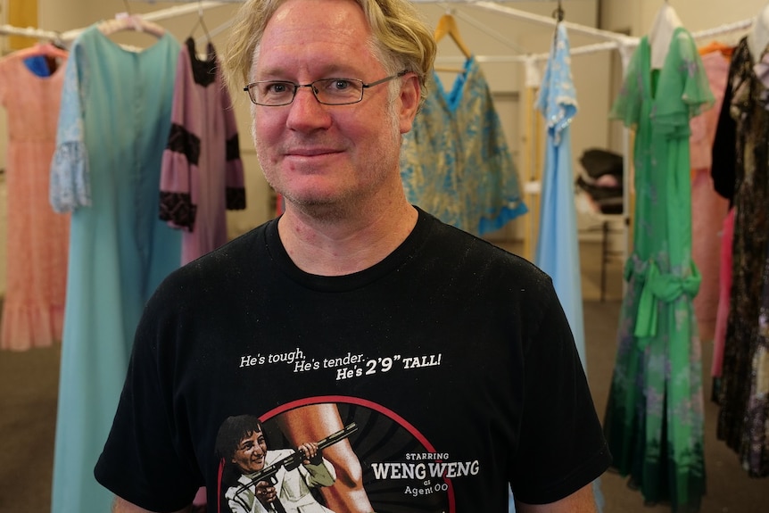 Steve Townson smiling, black shirt, standing in front of hanging dress collection.