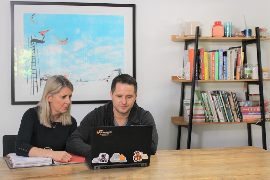 Couple sitting at laptop computer, beside bookcase