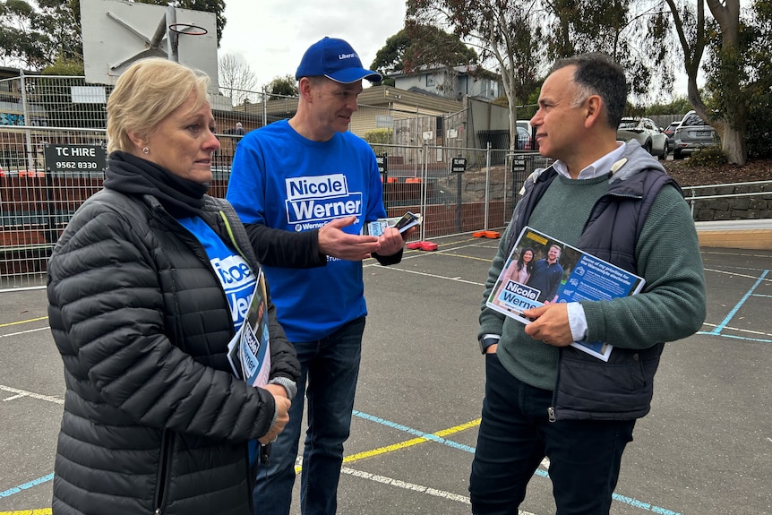 John Pesutto stands in a school playground, holding voting cards for Nicole Werner.