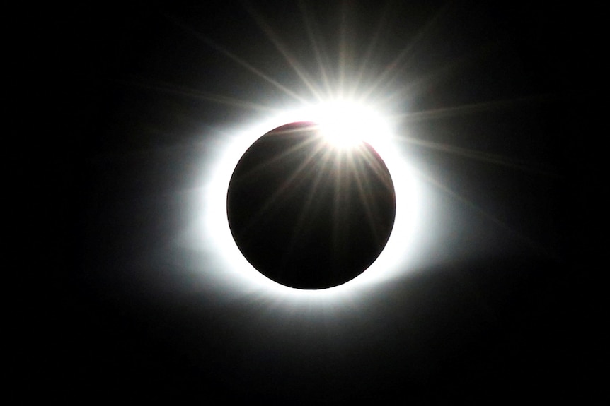 A dark circle is ringed by bright white light in a dark sky.