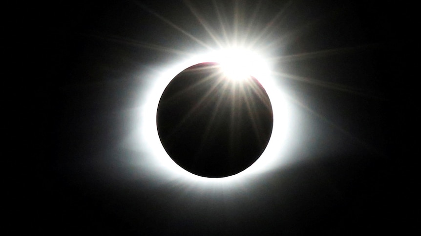 A dark circle is ringed by bright white light in a dark sky.