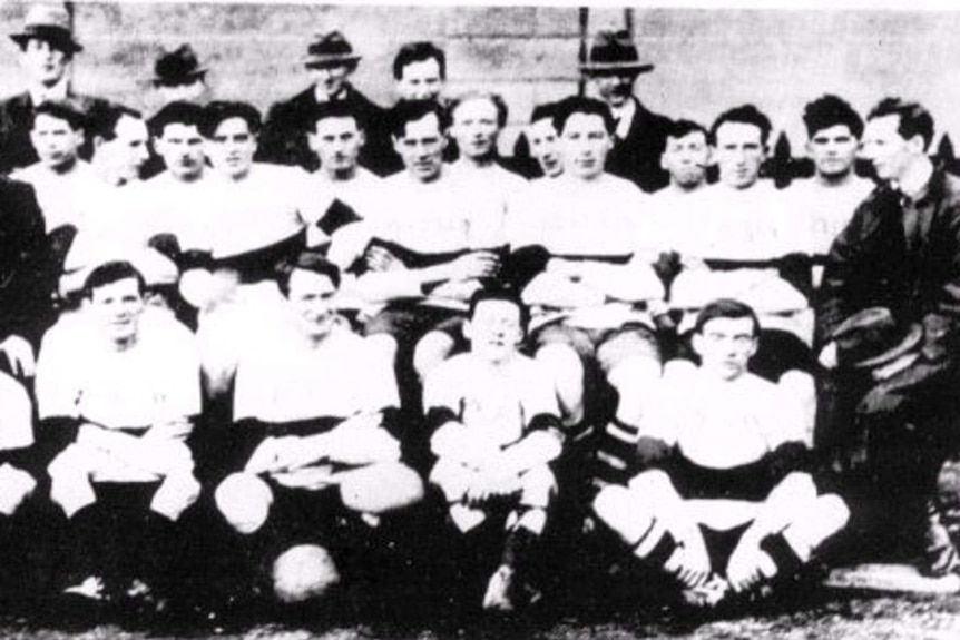 A black and white photo of a group of men posing in front of a wall