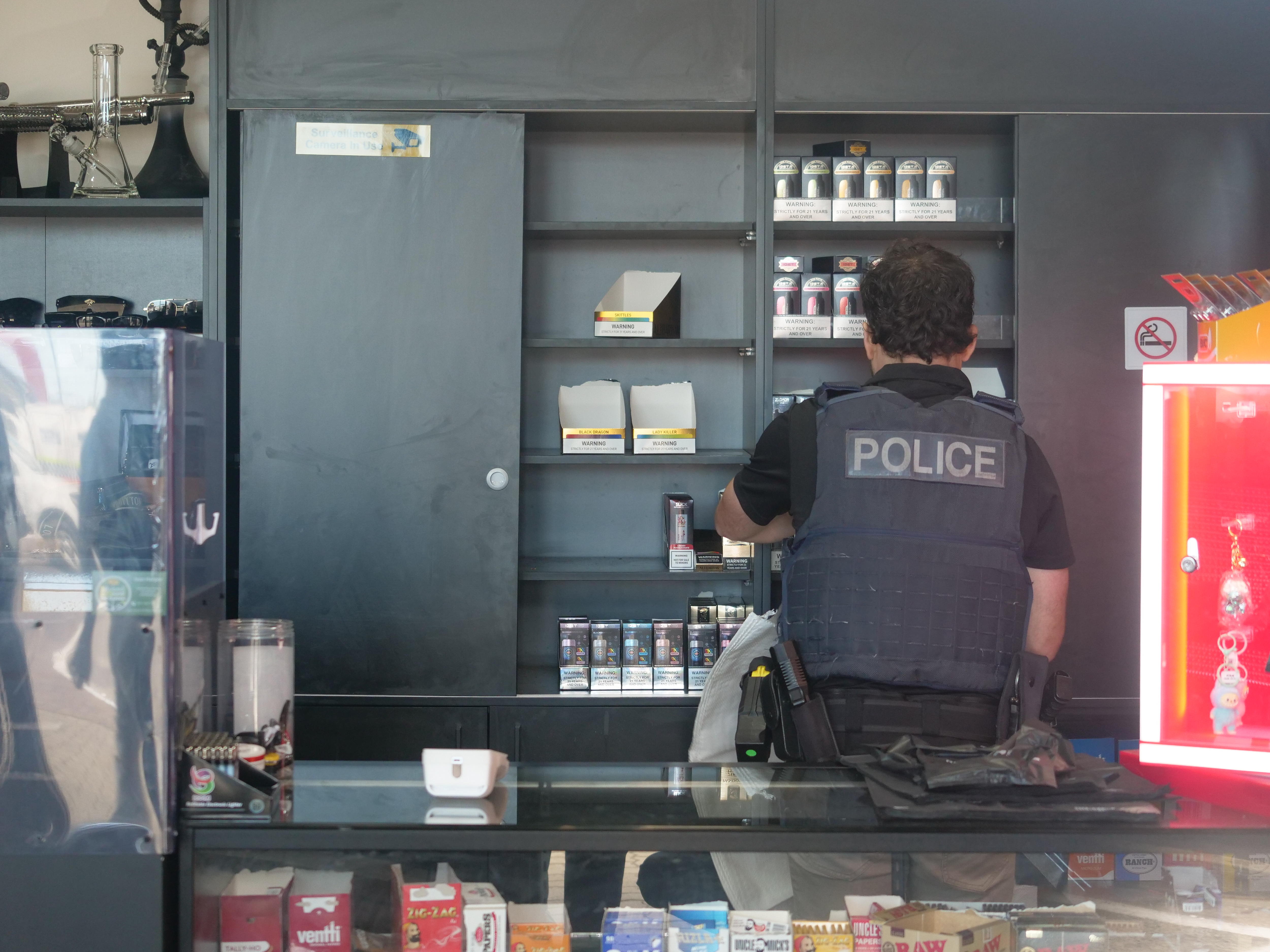 Um policial no balcão de uma tabacaria olhando dentro de um armário.