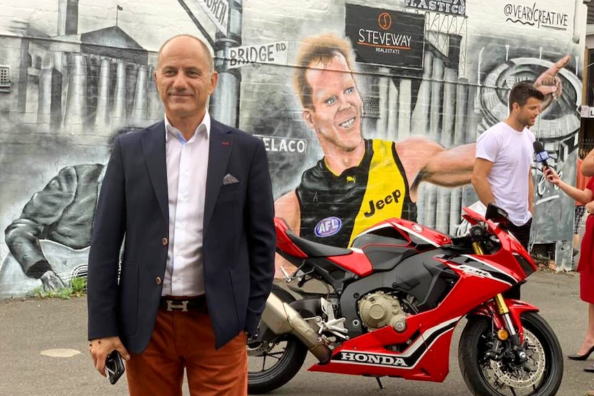 Steve Pantelios standing in front of a Honda motorcycle and a street art mural in Melbourne.