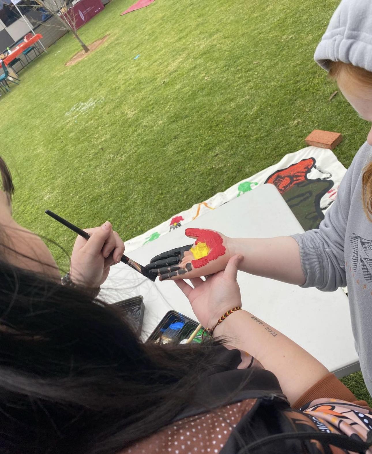Woman painting young girl's hand with Aboriginal flag