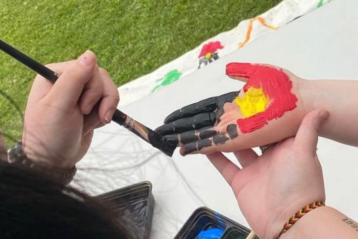 Woman painting young girl's hand with Aboriginal flag