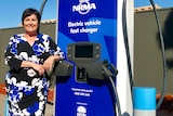 a white woman with black hair and a blue dress standing next to an electric vehicle charging station