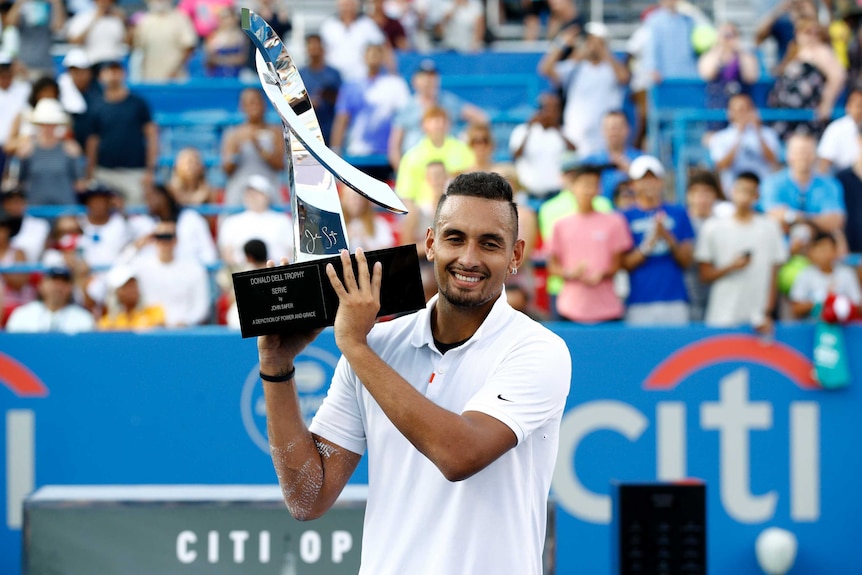 A male tennis player smiles as he holds a trophy after winning a tournament.