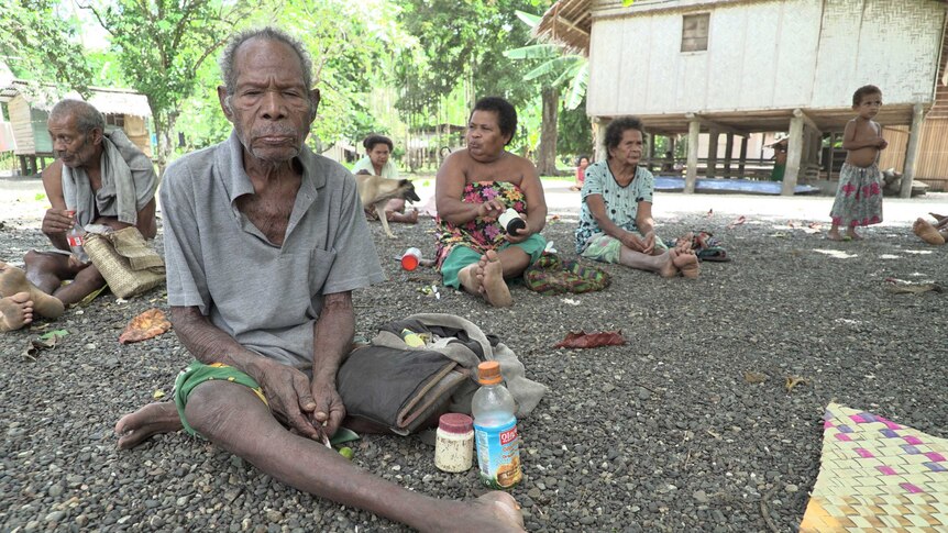 Lolo Tubaiodi sits with members of his family on pebbled ground in his village