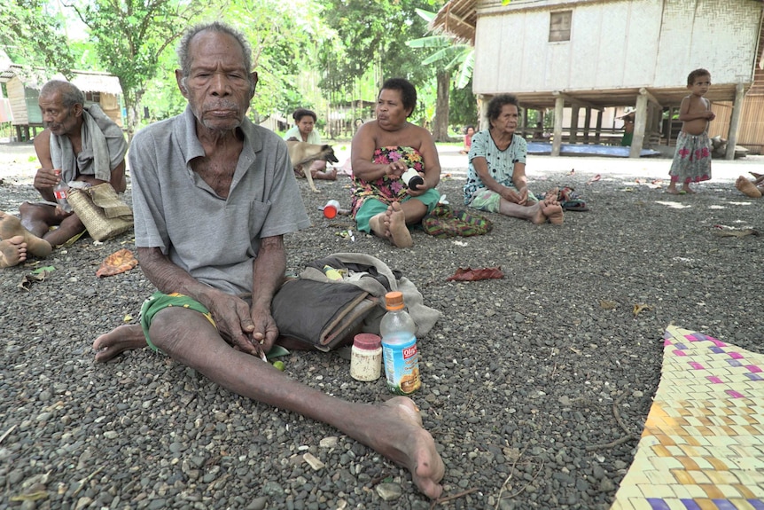 Lolo Tubaiodi sits with members of his family on pebbled ground in his village