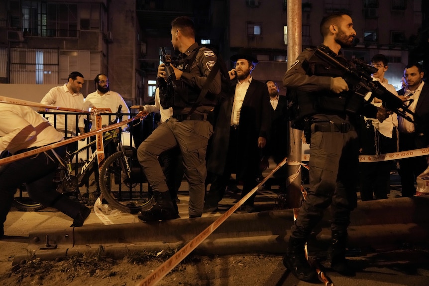Police stand next to a crowd holding semi-automatic guns