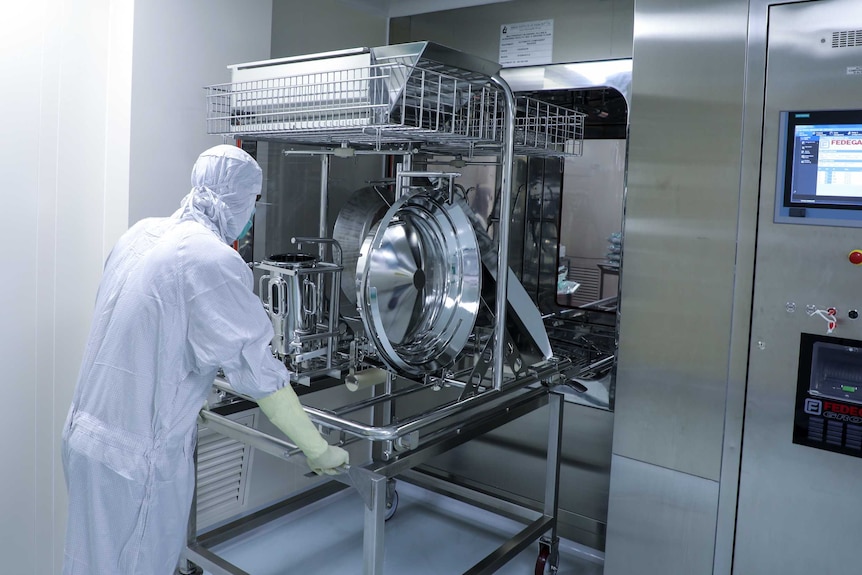 A man in full PPE pushes a trolley loaded with medical equipment