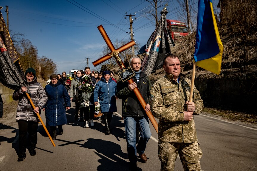 Villagers carry a large cross and Ukrainian flag. 