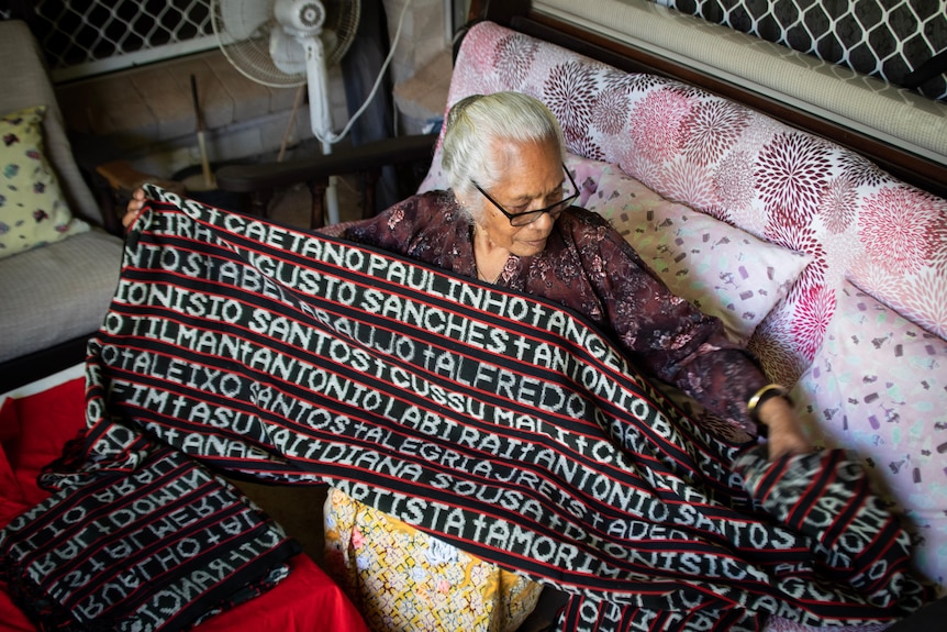 A woman holding woven tais with the names of massacre victims.
