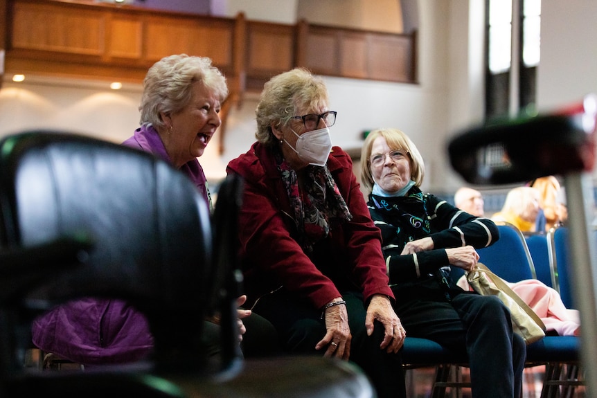 Older women laughing, one without a mask, one with a mask, and one with mask down